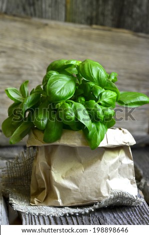 Bunch of basil in paper bag on wooden table.