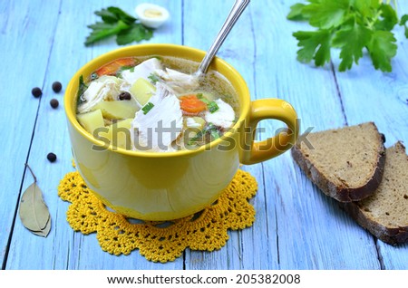 Potato soup with chicken in a yellow cup on the blue wooden table.