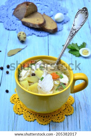 Potato soup with chicken in a yellow cup on the blue wooden table.