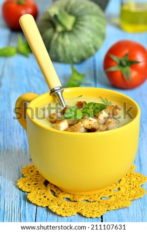 Zucchini cream soup with chicken and croutons  in a yellow cup.