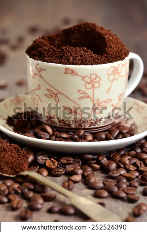 Ground coffee and coffee beans in a cup on wooden table.