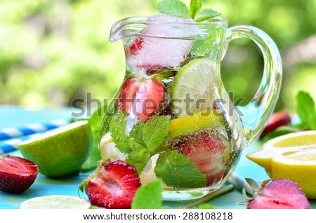 Fruit lemonade with strawberry in a pitcher on blue wooden table.