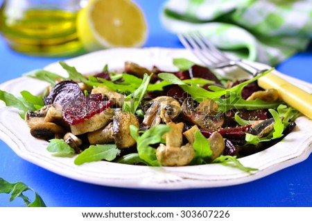 Beet salad with arugula and mushrooms on a white plate.