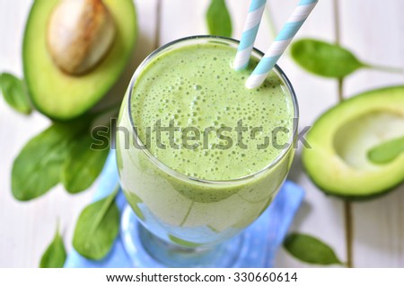 Avocado and spinach green smoothie on a light wooden table.