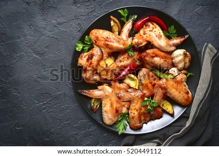 Grilled chicken wings on a black plate on a stone,concrete or slate background.Top view.