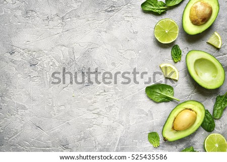 Avocado halves with lime slices and baby spinach leaves on a grey concrete,stone or slate background.Top view with copy space.