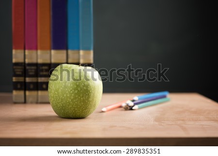 School books with apple on desk over green school board background