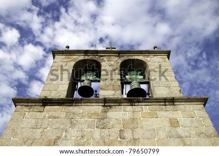 a medieval church bell tower with stone carved faces and two bells under a blue sky