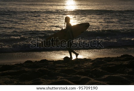 Young surfer silhouette walking on the beach with his surf board beside, Hawaii