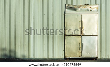 An Old Industrial Refrigerator Abandoned in Front of Green Corrugated Plate With Shadow of Trees