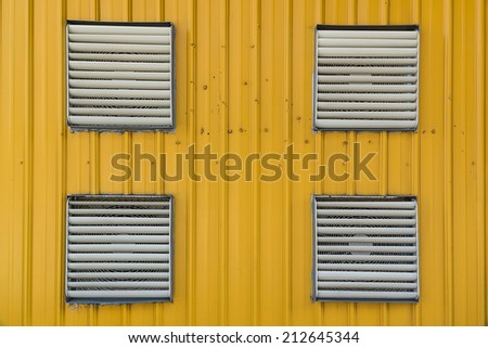 Four Shutter Windows Covering Exhaust Fans on The Wall of Yellow Corrugated Plate