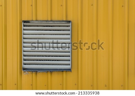 A Steel Shutter Window Covering A Exhaust Fan on The Wall of Yellow Corrugated Plate