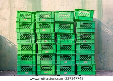 Pile of Green Plastic Baskets Stacked in Columns In Front of An Old Yellow Wall. The Sun Cast Shadow on The Wall From Upper Left.