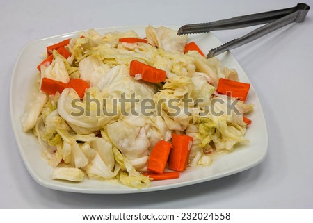 Pickled Cabbage and Carrot in White Plate with A Iron Clamp on S White Table.