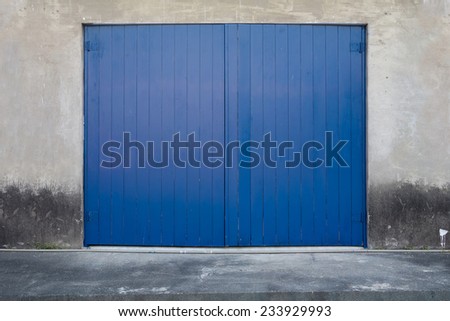 A Blue Wooden Door on Concrete Wall on A Concrete Platform. The Wall and Floor is Aged and Weathered.