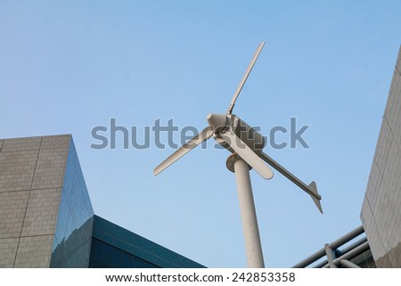 A Small Wind Power Generator in Front of A Modern Building, Against Blue Sky.