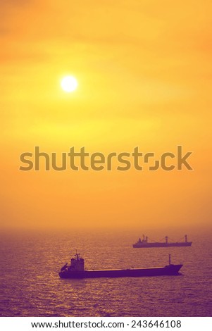 Two Cargo Ship Sailing in The Ocean in Heavy Mist Under Sunset. The Image is Post Processed With The Sky in Yellow and Orange Hues, and with Purple Hue on The Ships and The Ocean.