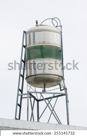 A Water Tank Made of Stainless Steel on Top of The Roof. The Middle Section of The Tank Are Painted in Green Color. Aged And Weathered.