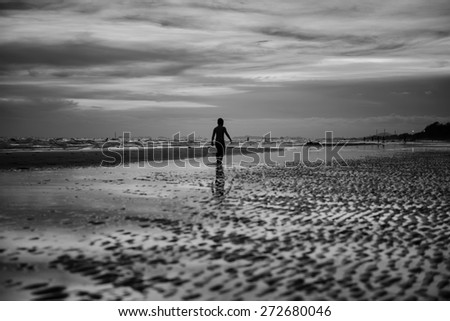 A boy walks on the beach silhouette sunset at seaside alone black and white tone.
