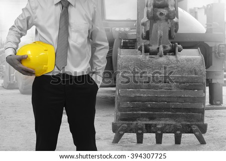 Safety Construction Concept , Safety engineer holding yellow hardhat and Loader  backhoe  truck background.