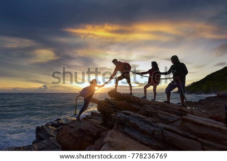 Male and female hikers climbing up silhouette mountain cliff . helps and team work concept.