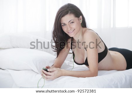 young cute girl smiling and listening to music with music player in lingerie while in bed