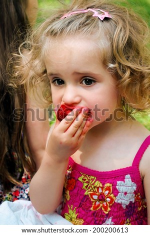 Blonde girl in summer dress eating strawberries. Stained face.
