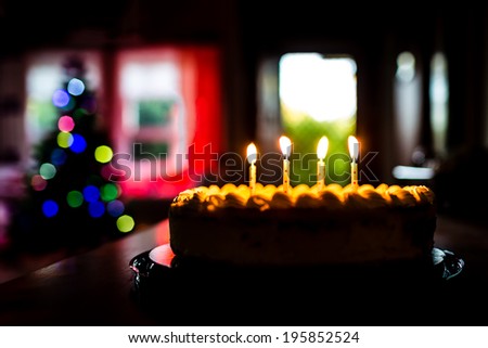 Four Years Old Birthday Celebration Event With Cake And Candles In A Home Environment. The bokeh background includes a front door and blurred Christmas tree lights.