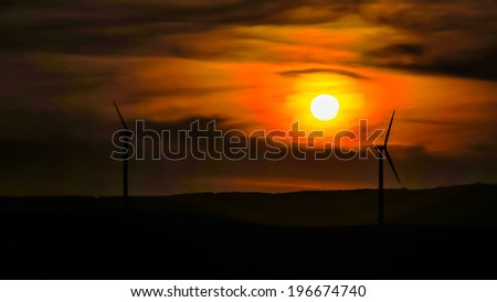 Wind turbine silhouette up on the hill against the background of the sun setting in the dramatic cloudy sky