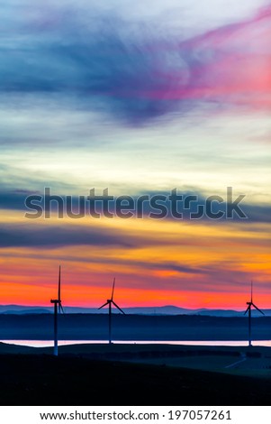 Wind turbines standing on the hills near the water shore in the dusk twilight