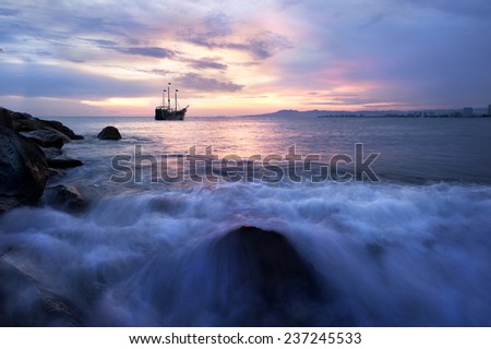 A Pirate Ship sails along the ocean at sunset as the waves roll into shore.