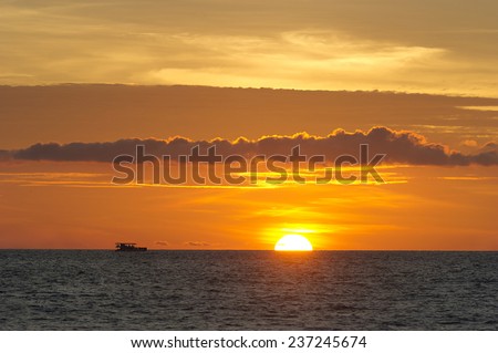An ocean ferry cruises along the water as the sun sets on the horizon.
