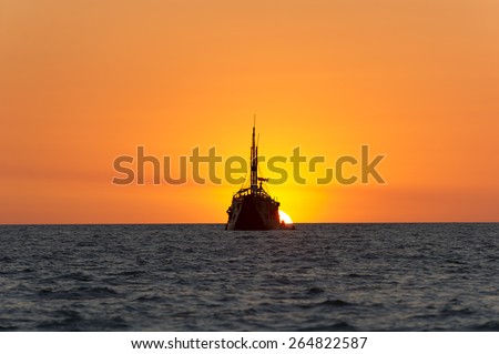 Ship old and wooden sits at sea with its mast and hull as a silhouette as it watches the surreal fantasy sun set in the background. This photograph was taken on the beach along the Pacific.