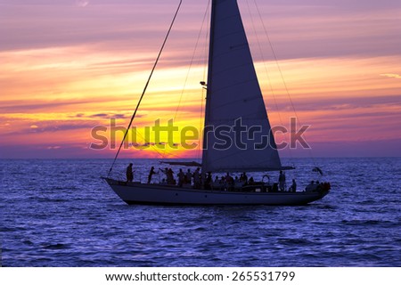 A Sailboat full of party people on vacation sails along the ocean as the sun sets in the background