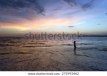 A boy reaches out to the setting setting sun as he stands in the ocean water.