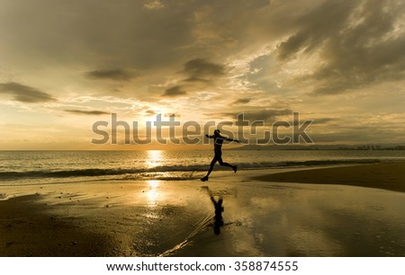 Runner silhouette is a man taking an athletic leap with an ocean sunset backdrop while running along the beach.