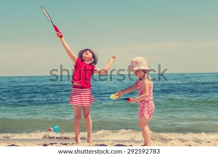 Funny little girls (sisters) play badminton on the beach. The image is tinted.