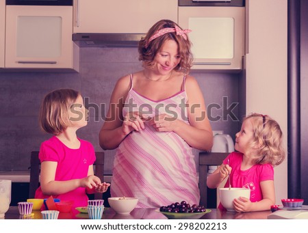 Pregnant mom with little daughters preparing cupcakes. Selective focus.