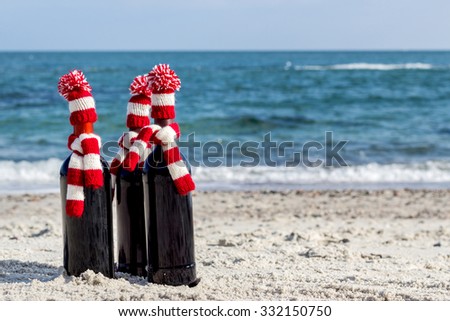 Christmas gifts. Three bottles of wine in knitted hats and scarves on the beach. Selective focus.