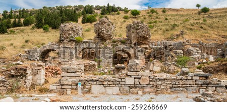 Ephesus, Turkey - May 19, 2010: Remains of three arches in front of a hill with dry grass and trees.