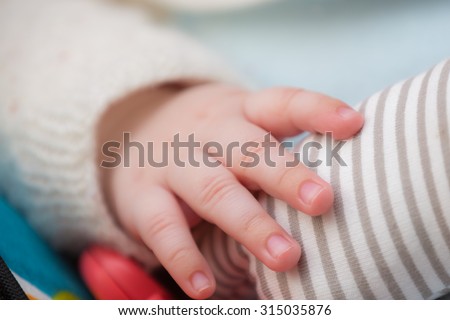 Close-up of the right hand fingers of a baby who wears a fleece jacket and is touching a toy.