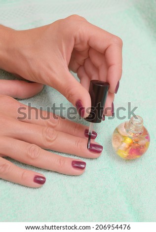 Female hand with stylish colorful nails, on color towel. Colorful oil bottles
