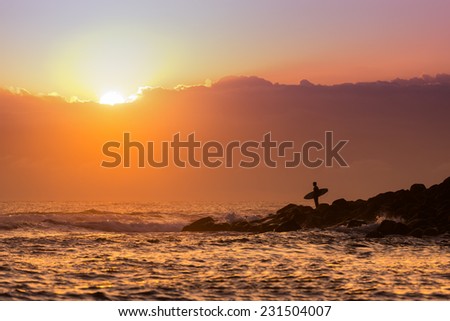 Surfer standing on the point with the sunrise in the background
