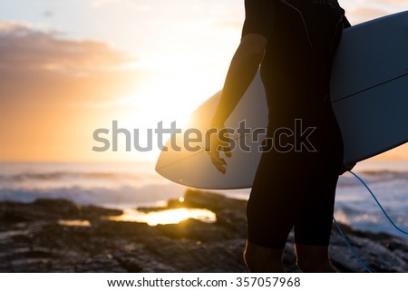 Surfer standing on the rocks at sunrise or sunset