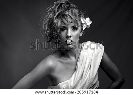landscape format duo tone beauty photograph of a young european woman with an origami flower in her mouth looking into camera.