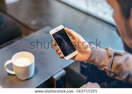 Hipster man sitting in cozy cafe and drinking coffee, Close-up of male hand using modern smart phone in cafe shop, blurred background, shallow DOF