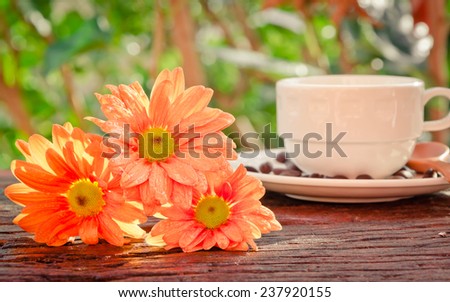 Orange gerbera flower and coffee cup on wooden table background with bokeh background vintage retro pastel tones.