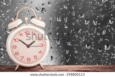 Alarm clock on wooden table with water drop on vivid color glass background soft focus.