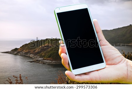 Woman hand holding smartphone against on nature of sea background soft focus.