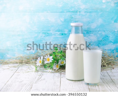 A bottle of rustic milk and glass of milk on a wooden table on blue background